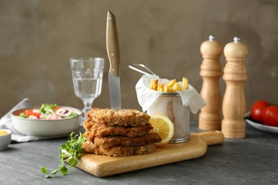 Tasty schnitzels served with knife and french fries on grey table