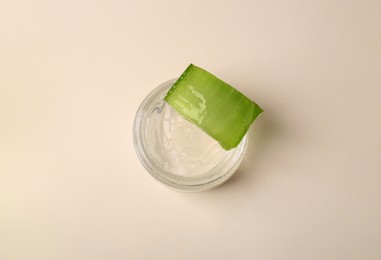 Jar of natural gel and cut aloe on beige background, top view