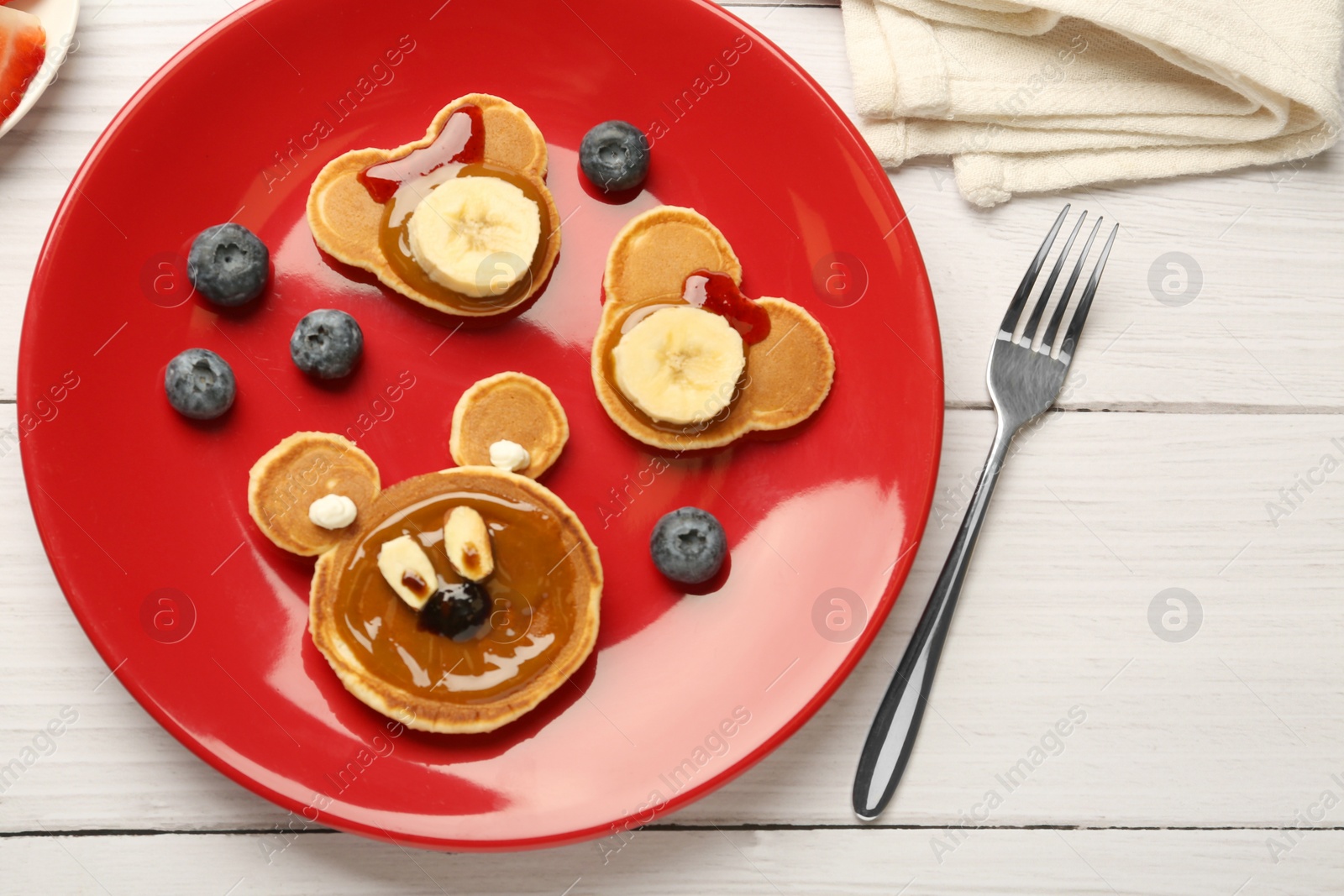 Photo of Creative serving for kids. Plate with cute bears made of pancakes, berries, banana and chocolate paste on white wooden table, flat lay