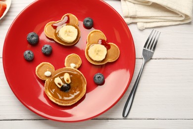 Creative serving for kids. Plate with cute bears made of pancakes, berries, banana and chocolate paste on white wooden table, flat lay