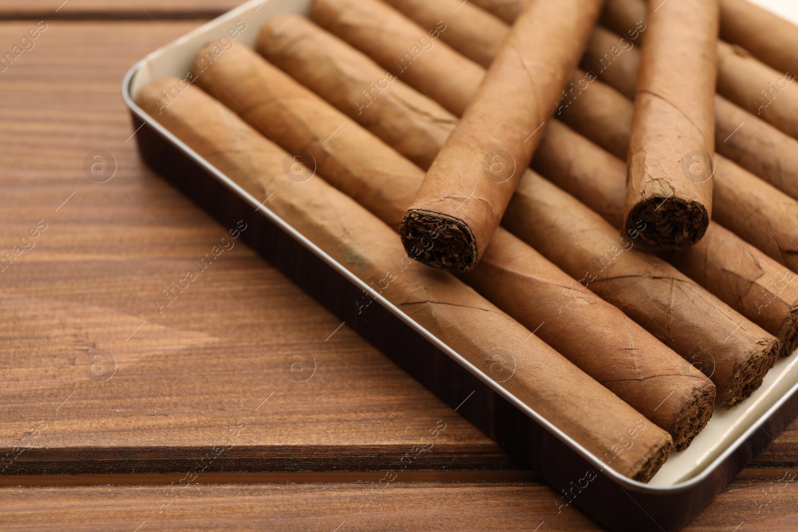 Photo of Many cigars in box on wooden table, closeup