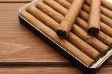 Photo of Many cigars in box on wooden table, closeup