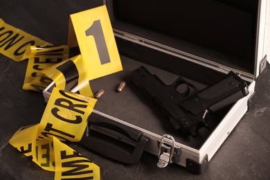 Photo of Open case with gun, bullets and crime scene marker on black table, closeup