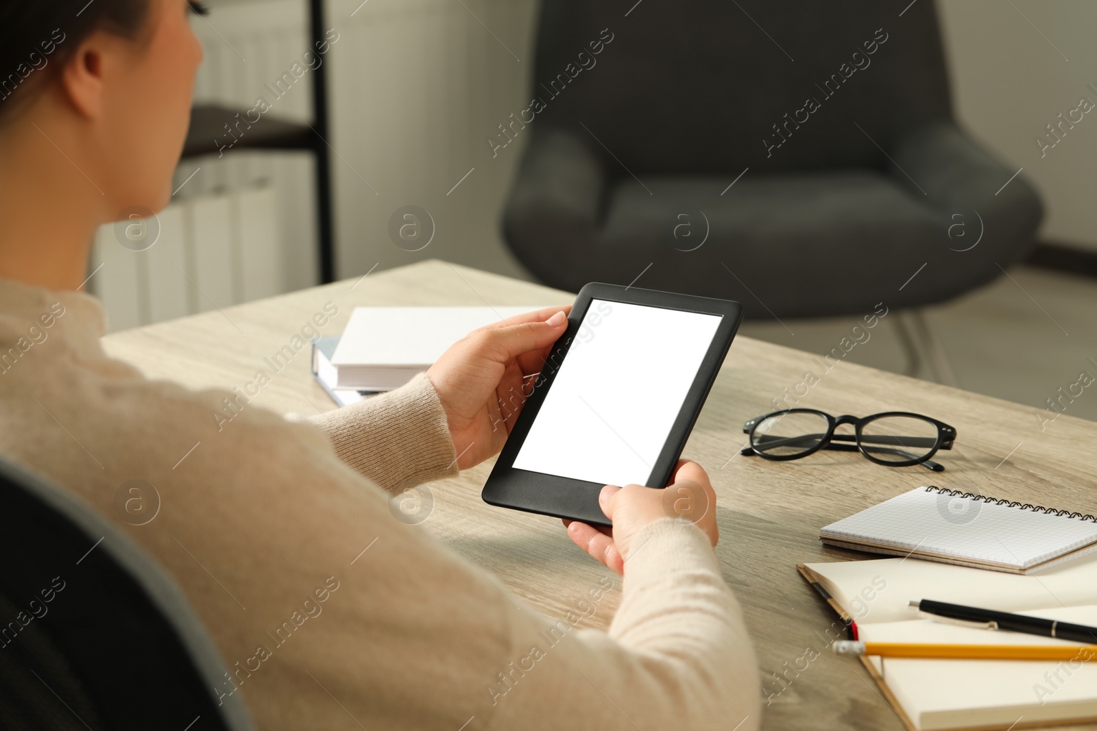 Photo of Young woman using e-book reader at wooden table indoors, closeup