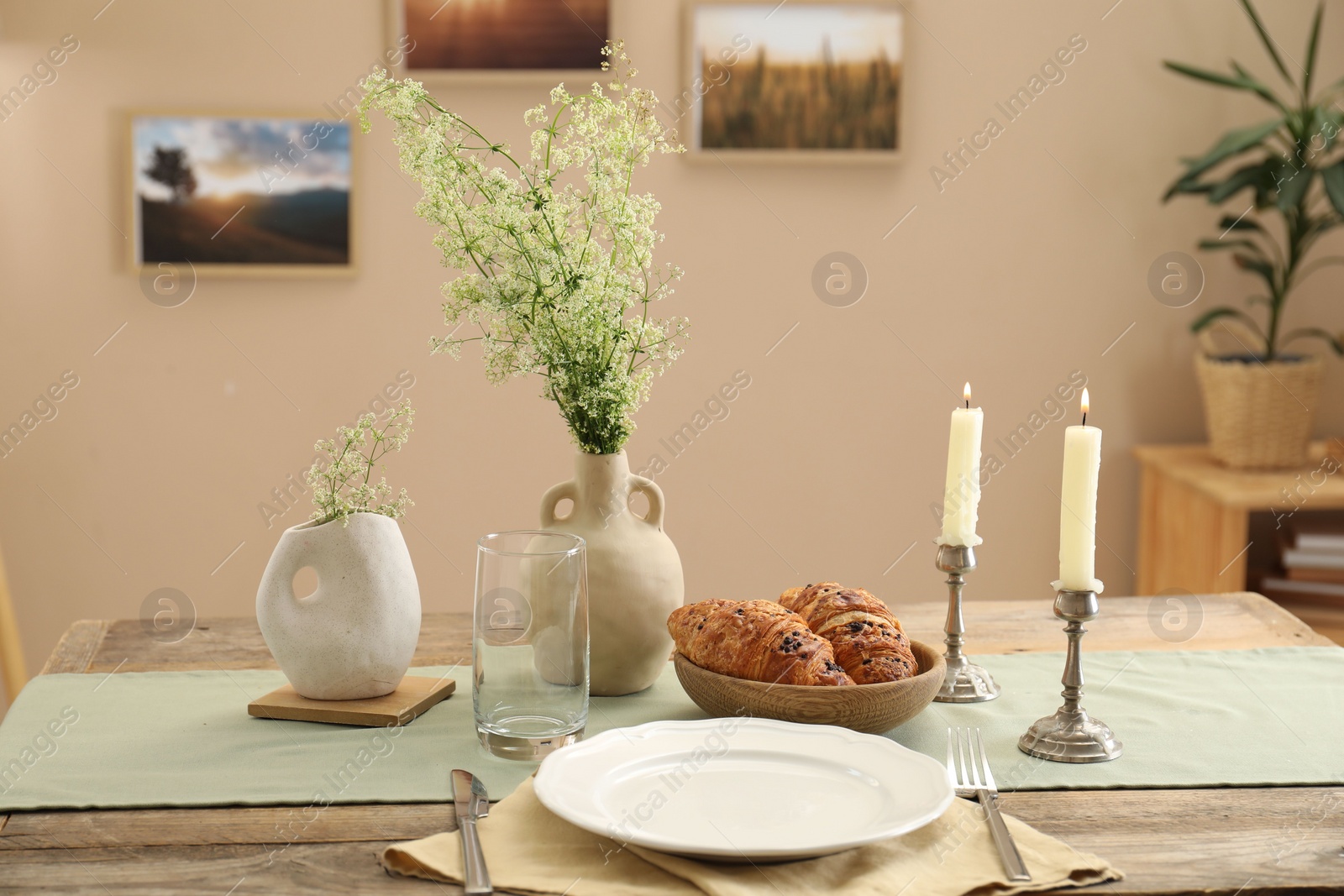 Photo of Clean tableware, candlesticks, flowers and fresh pastries on table in stylish dining room