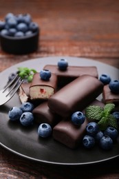 Photo of Delicious glazed curd snacks with fresh blueberries and mint served on wooden table, closeup