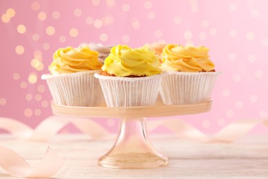 Stand with tasty cupcakes on white wooden table against blurred lights