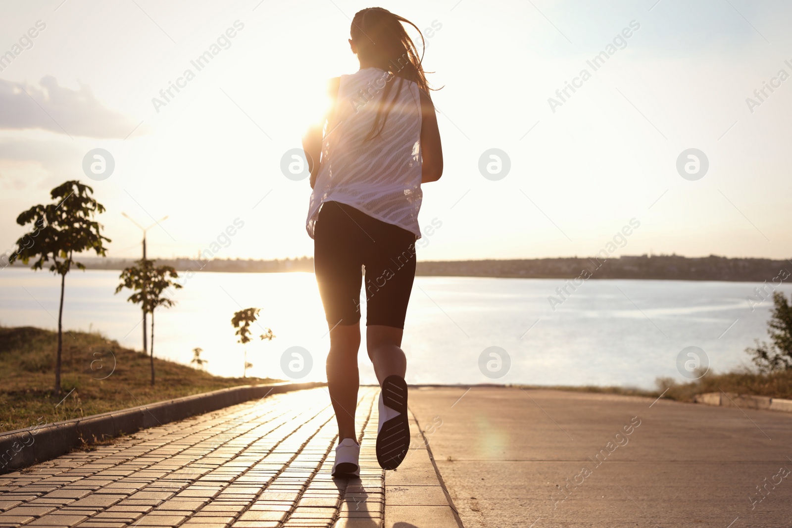 Photo of Young woman running near river in morning, back view