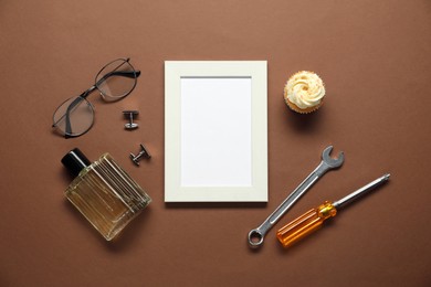Empty photo frame, cupcake and men accessories on brown background, flat lay with space for text. Father's day celebration