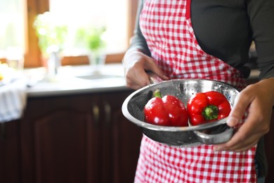 Photo of Woman holding colander with fresh bell peppers in kitchen, closeup. Space for text