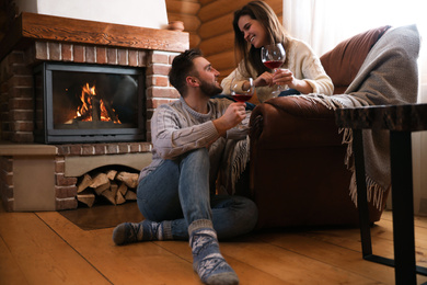 Lovely couple with glasses of wine near fireplace indoors. Winter vacation