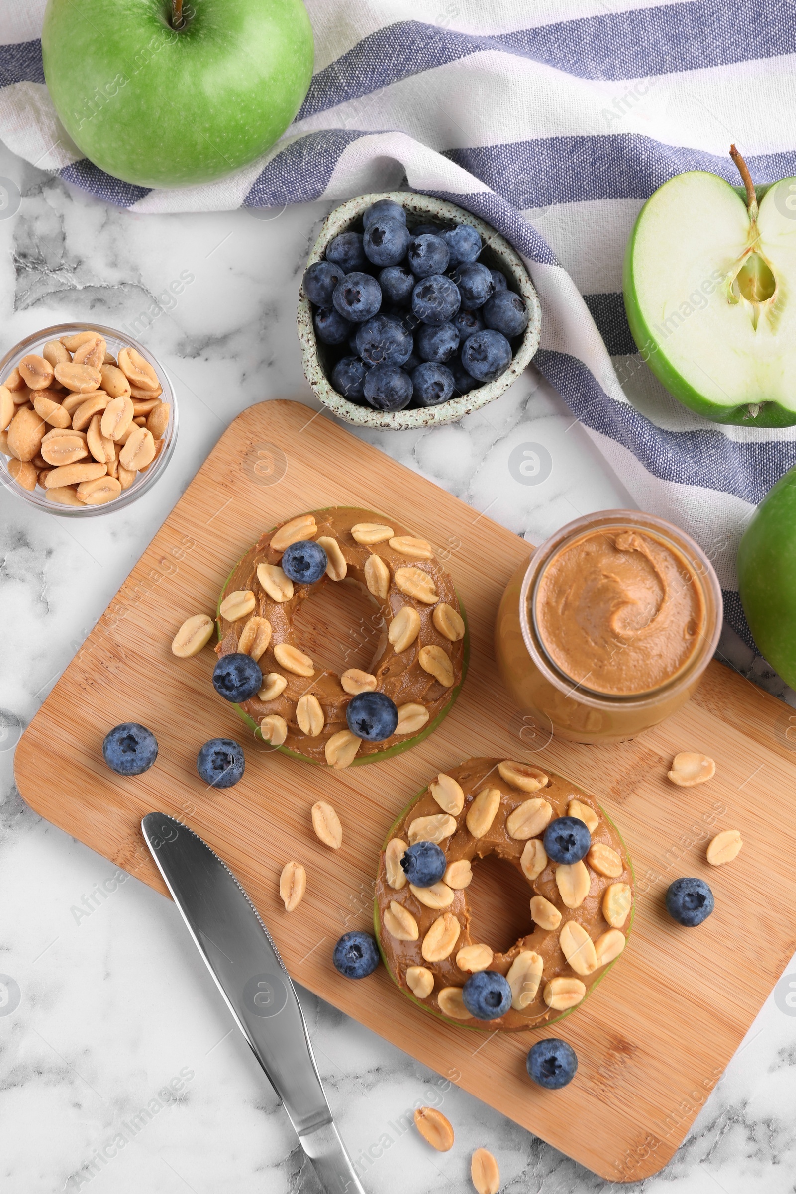 Photo of Fresh green apples with peanut butter, blueberries and nuts on white marble table, flat lay