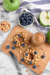 Photo of Fresh green apples with peanut butter, blueberries and nuts on white marble table, flat lay