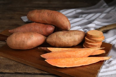Photo of Wooden board with cut and whole sweet potatoes on table