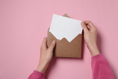 Photo of Woman taking card out of letter envelope at pink table, top view. Space for text