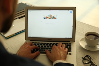 MYKOLAIV, UKRAINE - OCTOBER 27, 2020: Man using Google search engine on MacBook Air laptop at table indoors, closeup