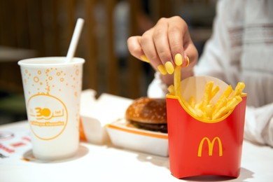Photo of WARSAW, POLAND - SEPTEMBER 04, 2022: Woman with McDonald's French fries, burger and drink at table in cafe, closeup