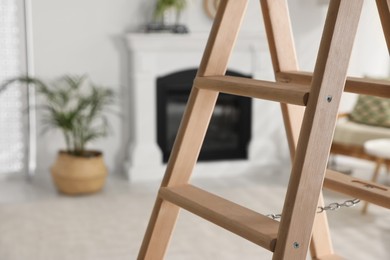 Photo of Wooden folding ladder in stylish living room, closeup. Space for text