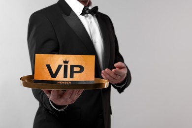 Man holding tray with VIP sign on light grey background, closeup. Space for text