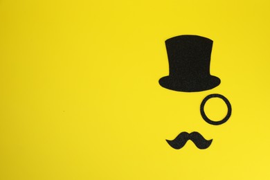 Photo of Man's face made of fake mustache, hat and monocle on yellow background, top view. Space for text