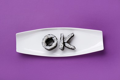 Word Ok made of sushi rolls on purple background, top view