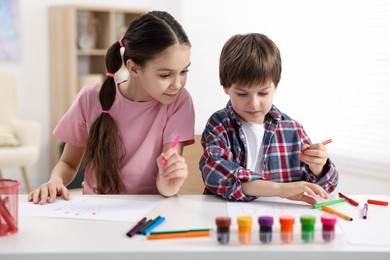 Happy brother and sister drawing at white table in room