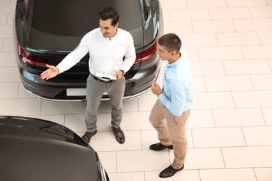 Young salesman working with client in modern car dealership, above view