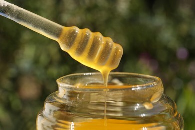 Photo of Taking delicious fresh honey with dipper from glass jar against blurred background, closeup