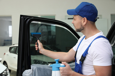 Worker washing tinted car window in workshop