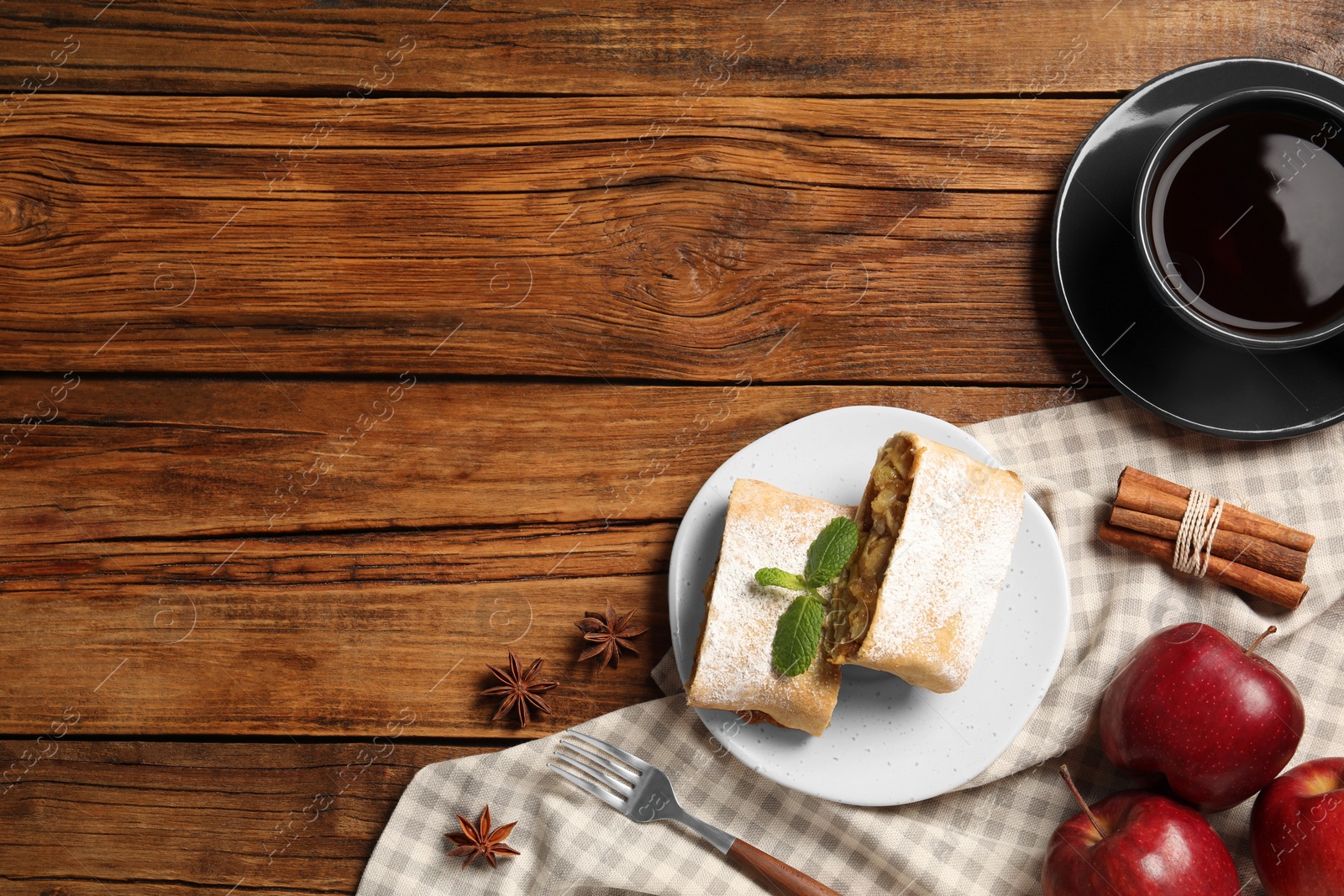 Photo of Delicious strudel with apples, nuts and raisins served on wooden table, flat lay. Space for text