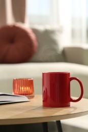 Red mug, book and burning candle on wooden table indoors. Mockup for design