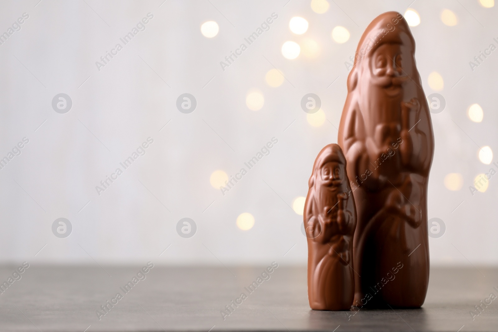 Photo of Small and big chocolate Santa Claus candies on light background with blurred Christmas lights