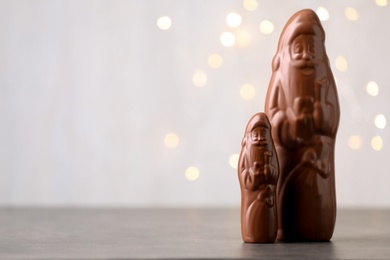 Small and big chocolate Santa Claus candies on light background with blurred Christmas lights