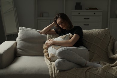 Sad young woman sitting on sofa at home