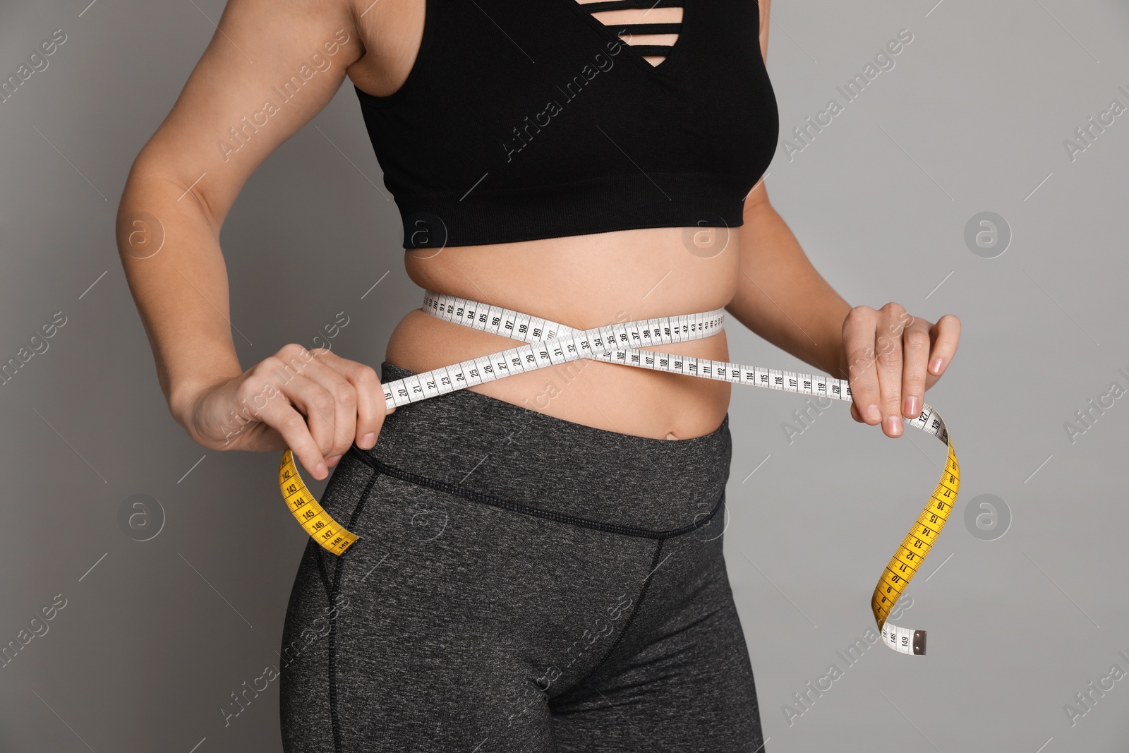 Photo of Woman measuring waist with tape on grey background, closeup