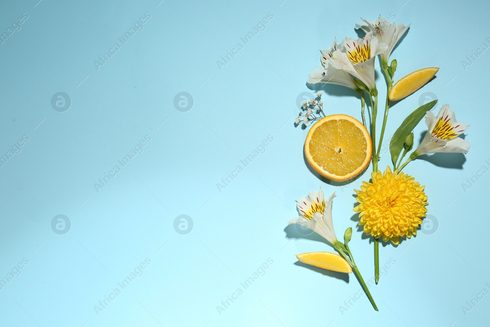 Photo of Flat lay composition with alstroemeria flowers and orange slices on light blue background, space for text