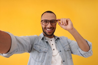 Smiling young man taking selfie on yellow background