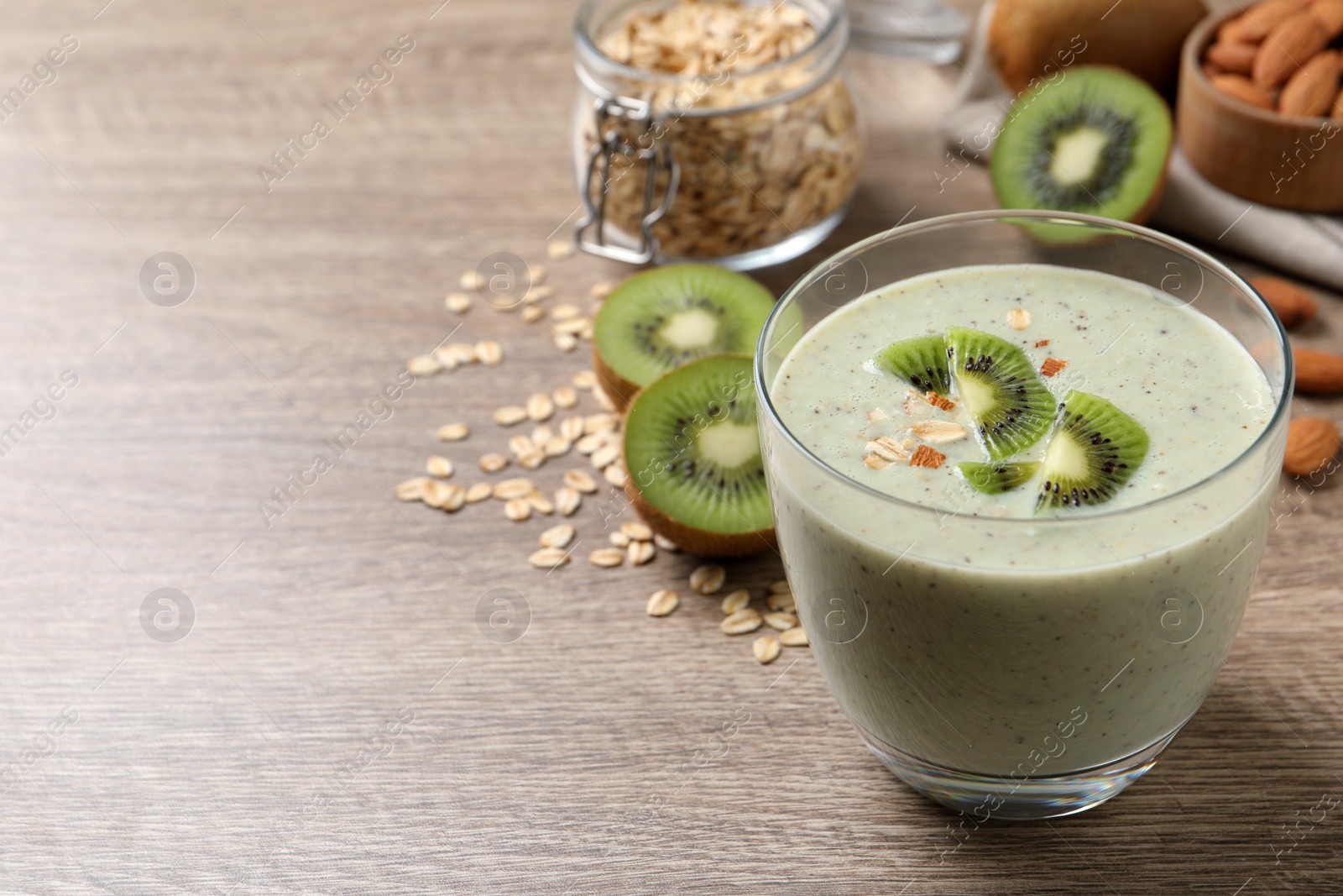 Photo of Glass of tasty kiwi smoothie with oatmeal on wooden table. Space for text