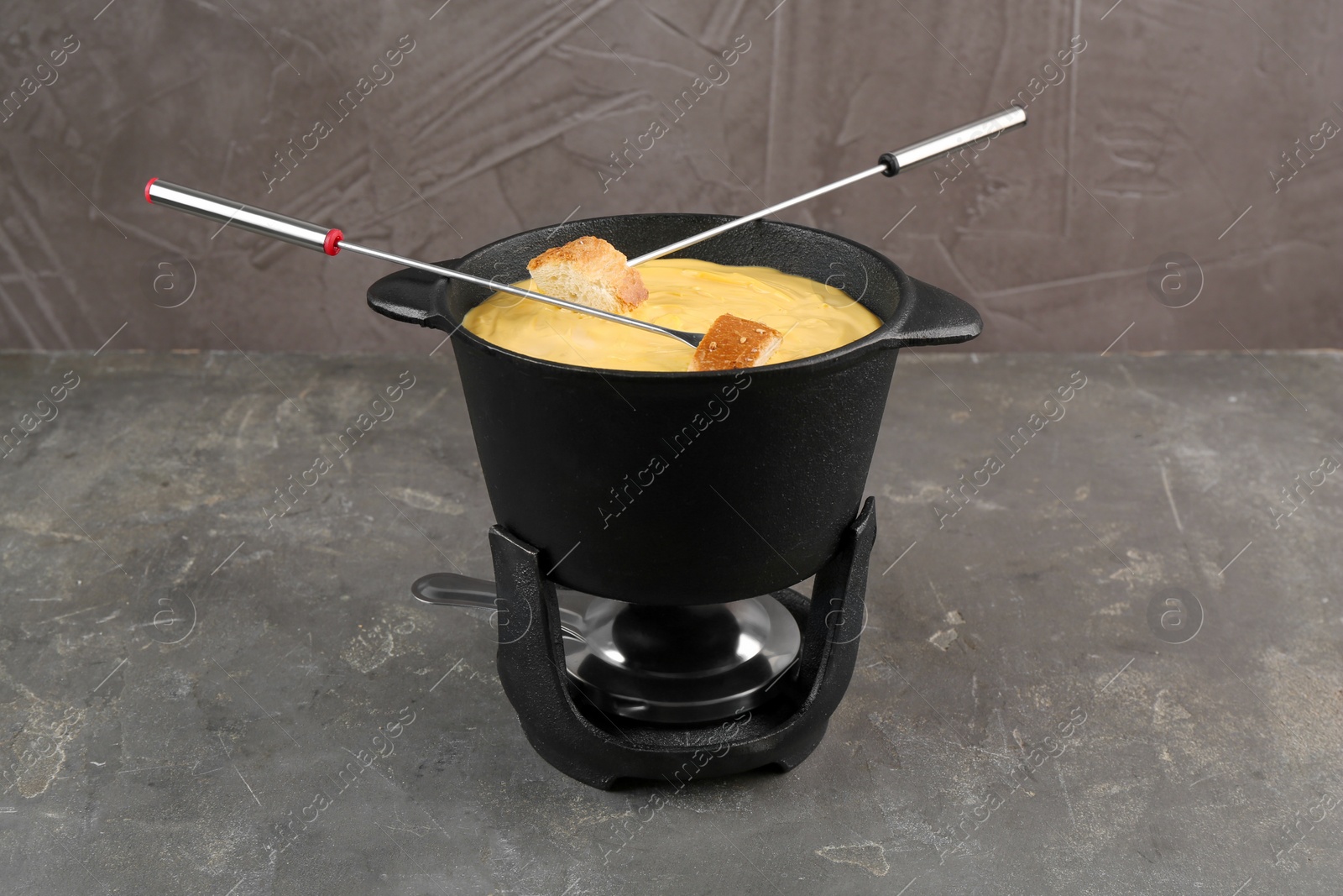 Photo of Fondue pot with tasty melted cheese, forks and bread on grey table