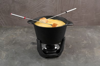 Photo of Fondue pot with tasty melted cheese, forks and bread on grey table