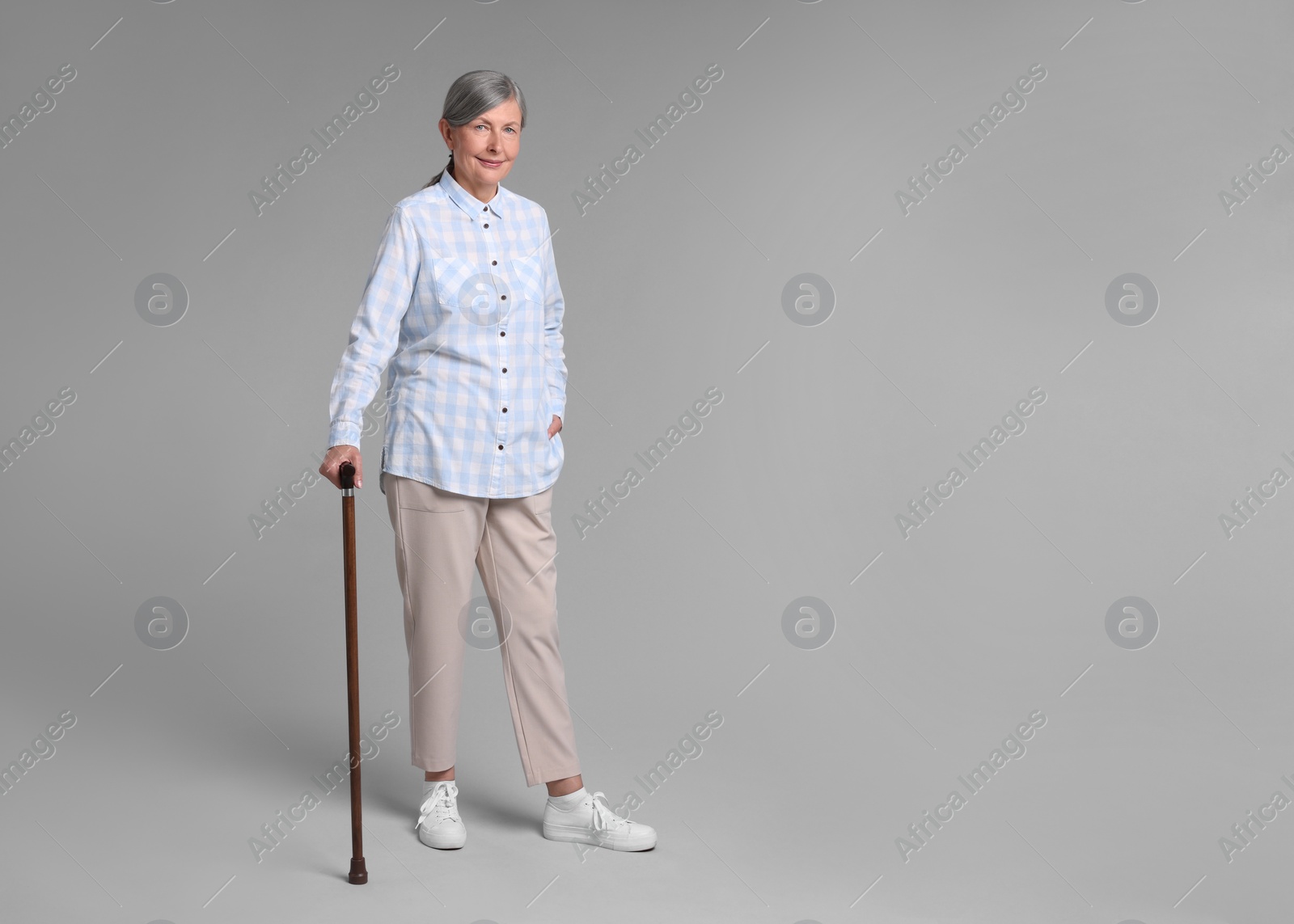 Photo of Senior woman with walking cane on gray background