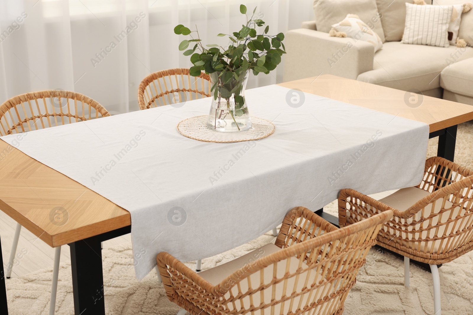 Photo of Vase with eucalyptus branches on table and chairs in dining room