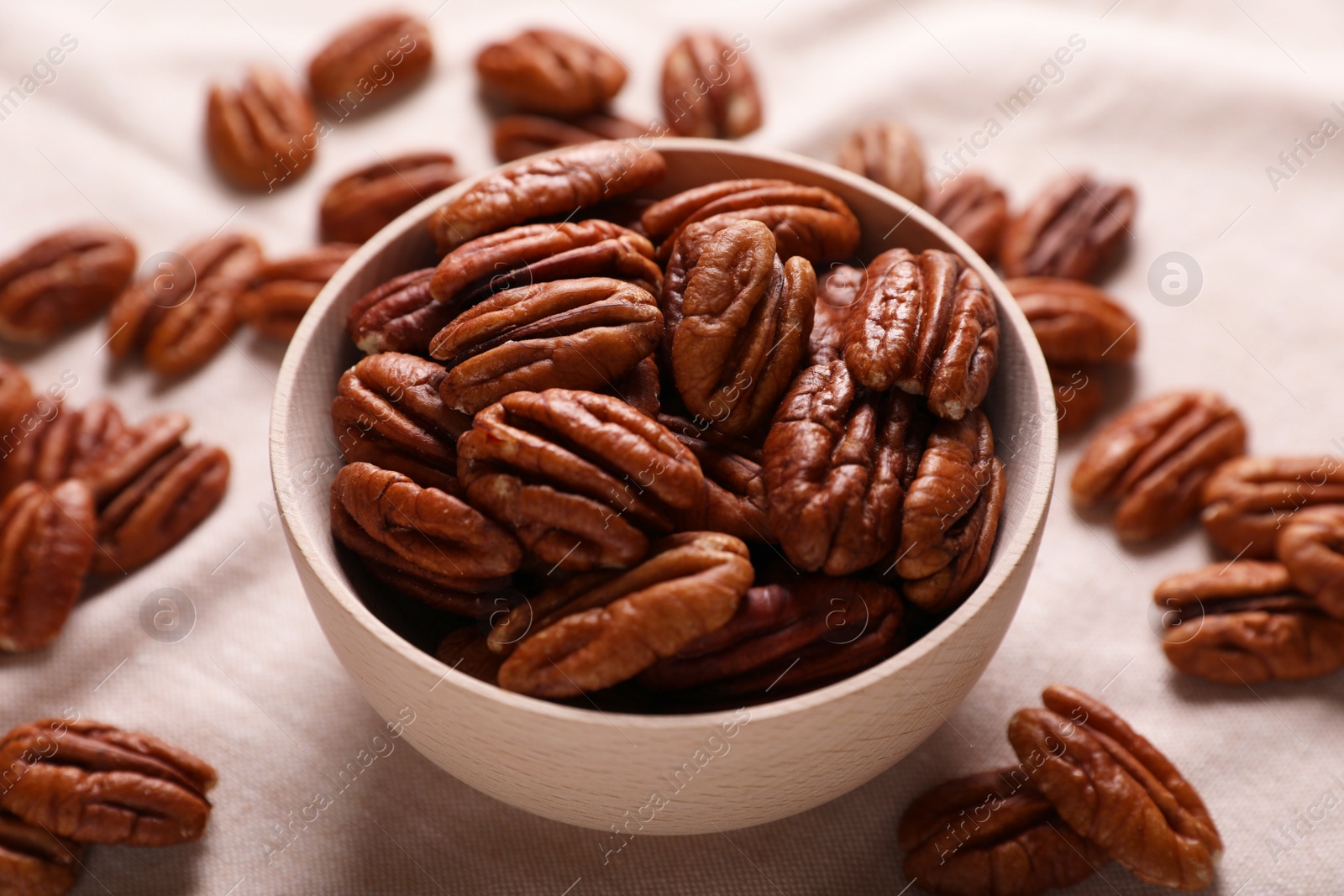 Photo of Tasty pecan nuts with bowl on beige cloth, closeup