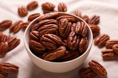 Tasty pecan nuts with bowl on beige cloth, closeup