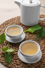 Photo of Green tea in white cups with leaves and teapot on table