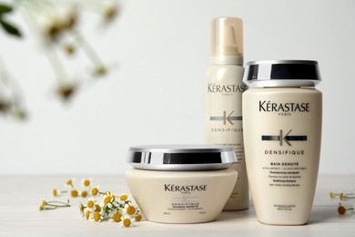 Photo of MYKOLAIV, UKRAINE - SEPTEMBER 07, 2021: Set of Kerastase hair care cosmetic products and chamomile flowers on white wooden table