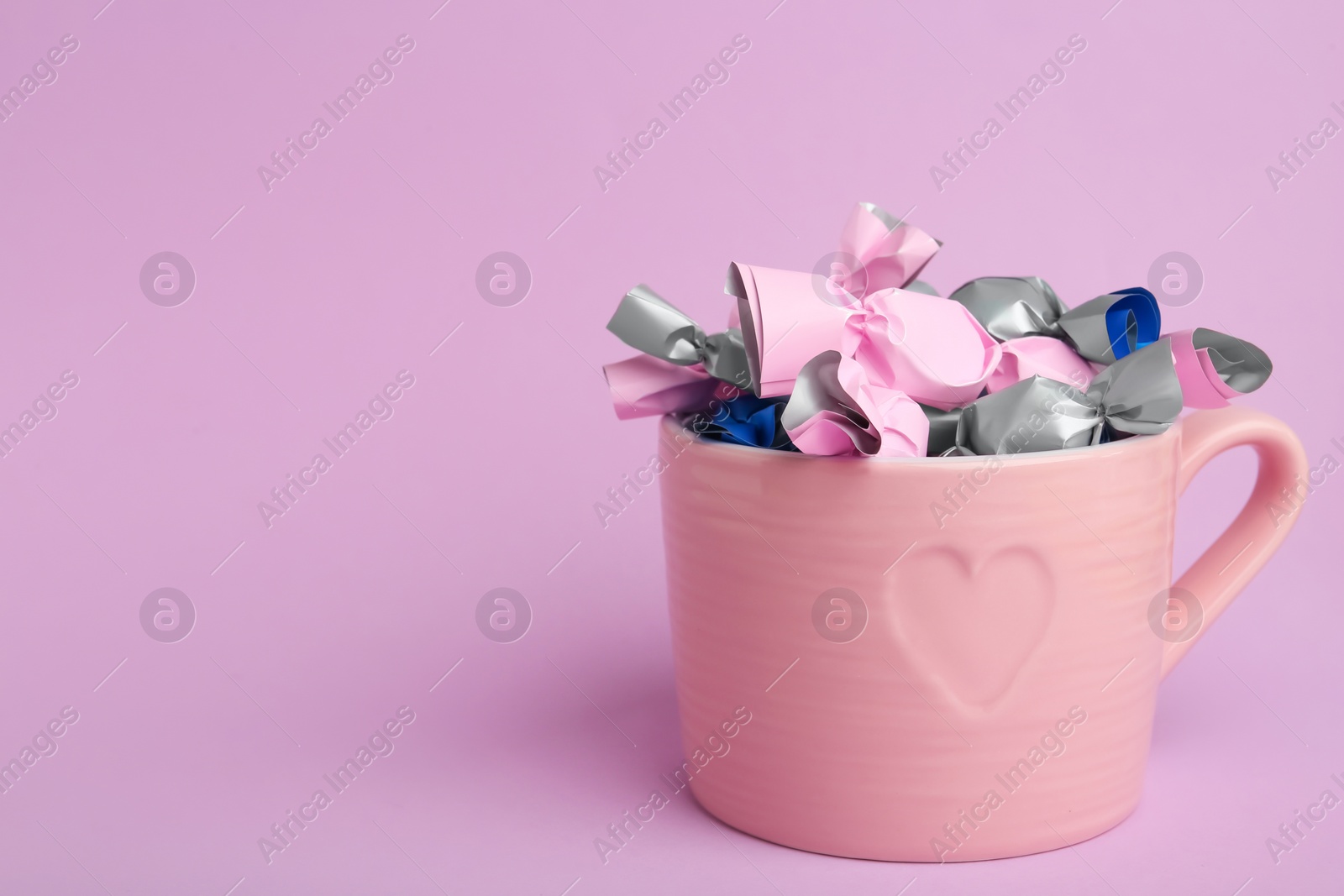 Photo of Candies in colorful wrappers on pink background. Space for text