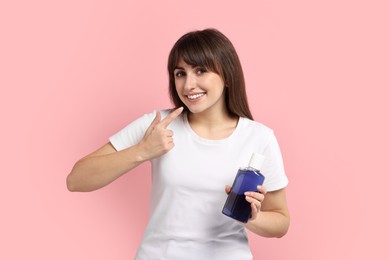 Photo of Young woman with mouthwash pointing at her healthy teeth on pink background