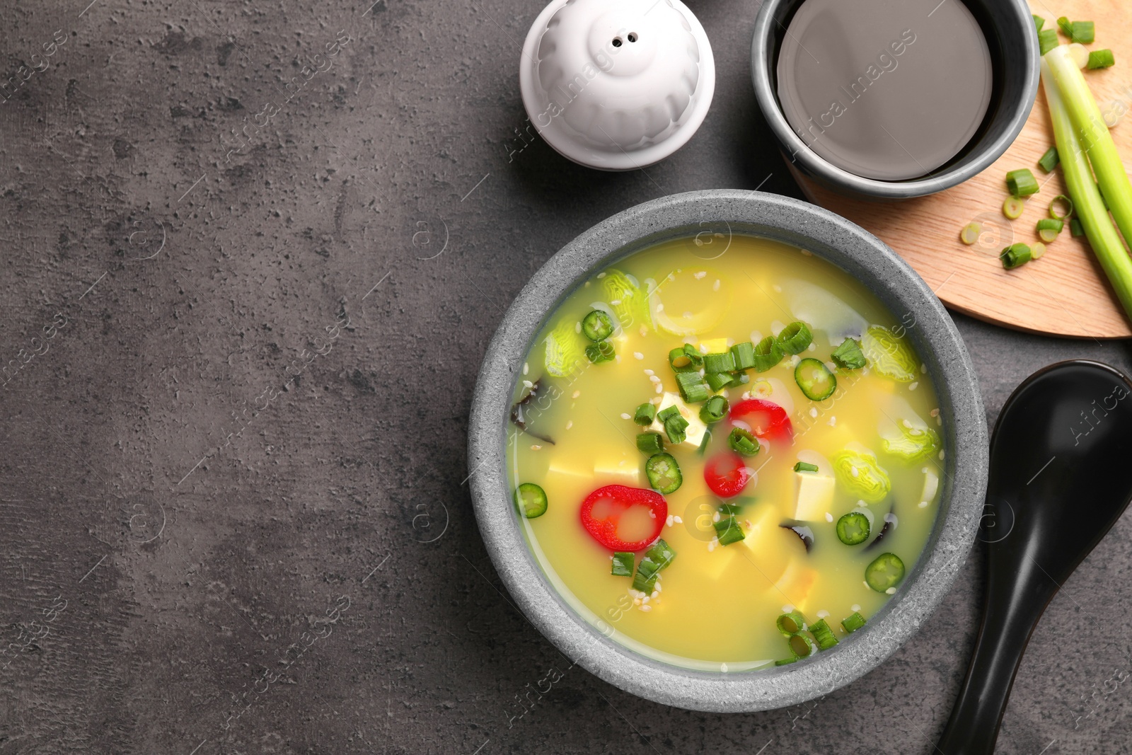 Photo of Bowl of delicious miso soup with tofu served on grey table, flat lay. Space for text