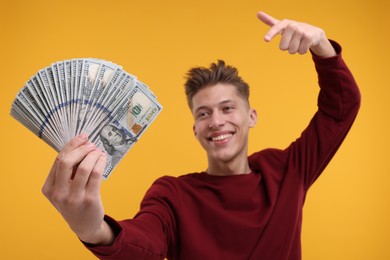 Happy man pointing at dollar banknotes on yellow background, selective focus